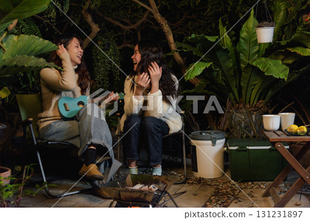 Winter camp outdoor friend people forest woman happy, enjoying music with ukulele and warm fire, sharing cheerful laughter moments in cold evening during beautiful winter season vacation. Winter camp outdoor friend people forest woman happy, enjoying music with ukulele and warm fire, sharing cheerful laughter moments in cold evening during beautiful winter season vacation. 131231897