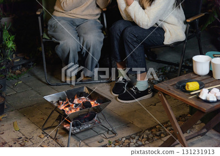 Winter camp outdoor, happy women friends enjoy forest evening, people gather around warm glowing fire pit, roasting delicious corn and sweet marshmallows, creating cozy winter memories. 131231913