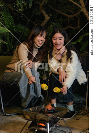 Winter camp outdoor friends people forest women happy, young women enjoy night grilling corn cob over warm coals, sharing laughter, creating cherished memory during cold winter evening. Winter camp outdoor friends people forest women happy, young women enjoy night grilling corn cob over warm coals, sharing laughter, creating cherished memory during cold winter evening. 131231914
