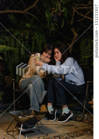 Winter camp outdoor, happy women friends enjoy forest night, people gather around fire pit, cozy warm sweaters create atmosphere during winter evening. Winter camp outdoor, happy women friends enjoy forest night, people gather around fire pit, cozy warm sweaters create atmosphere during winter evening. 131231917