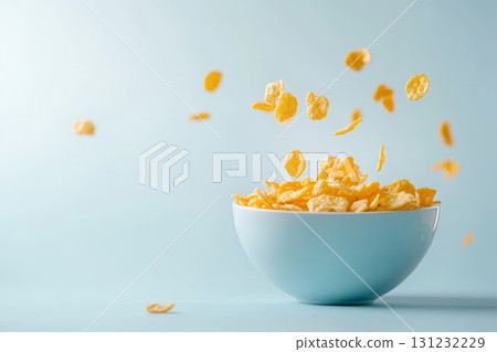 Golden corn flakes floating and falling into a light blue ceramic bowl against a pale blue background Golden corn flakes floating and falling into a light blue ceramic bowl against a pale blue background 131232229