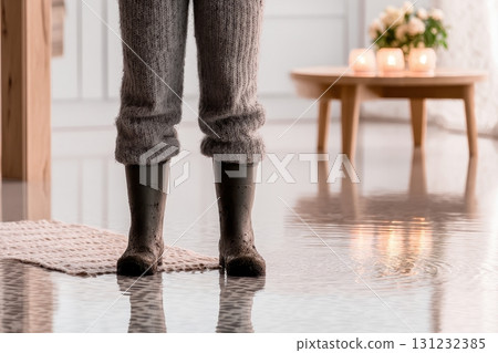 A person in grey knitted trousers and muddy boots stands in floodwater inside a home, highlighting the effects of water damage 131232385