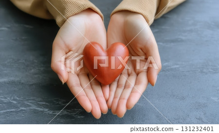 Woman's hands gently hold a small, heart-shaped, red object, symbolizing care and compassion 131232401
