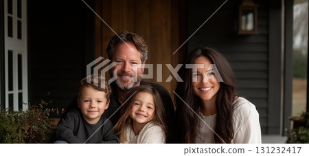 Happy family of four smiles warmly on their home's porch, showcasing family togetherness and happiness Happy family of four smiles warmly on their home's porch, showcasing family togetherness and happiness 131232417