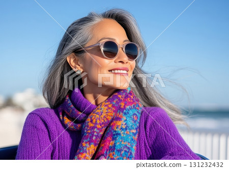 A stylish mature woman with gray hair enjoys a sunny day, wearing sunglasses and a vibrant purple sweater with a colorful scarf 131232432