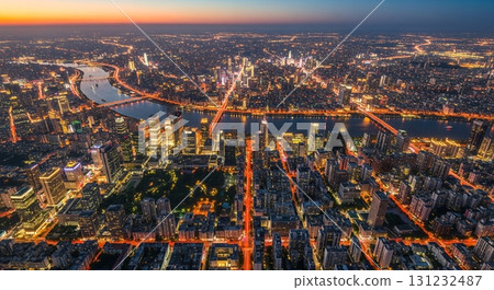 An aerial cityscape at night showcases a stunning river running through illuminated buildings and bridges, painting a beautiful picture of urbanization and infrastructure 131232487