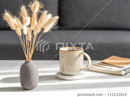 Beige cup of coffee on a light table with soft shadows, vase and notebook Beige cup of coffee on a light table with soft shadows, vase and notebook 131232610