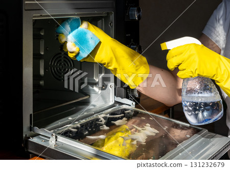 A person wearing yellow rubber gloves is cleaning an oven 131232679