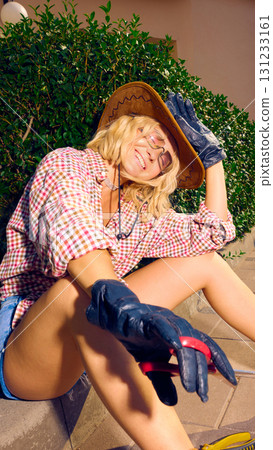 Stylish woman in cowboy hat smiling and relaxing on pavement with scissors in hand Stylish woman in cowboy hat smiling and relaxing on pavement with scissors in hand 131233161