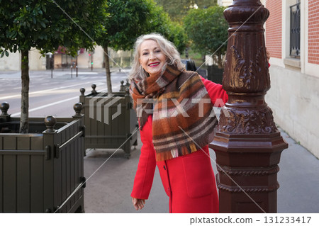 Gray-haired woman of sixty years old in a red coat and a terracotta scarf in the city 131233417