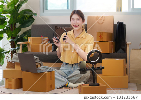 Content Creation. Young woman preparing for a live stream surrounded by packages. 131233567
