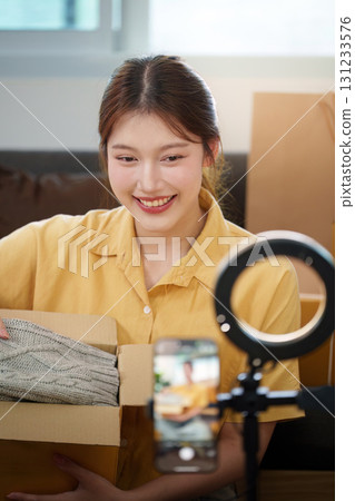 Unboxing Experience. Young woman revealing contents of a package during a live stream. Unboxing Experience. Young woman revealing contents of a package during a live stream. 131233576