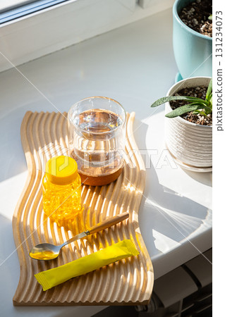 Yellow vitamins bottle, spoon, water glass, powder sachet on wooden board. 131234073
