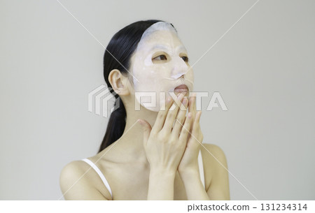 Young woman applying sheet mask Young woman applying sheet mask 131234314