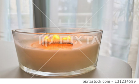 Large scented candle in glass jar burning in cozy autumn home interior, warm hygge atmosphere, aromatherapy 131234589