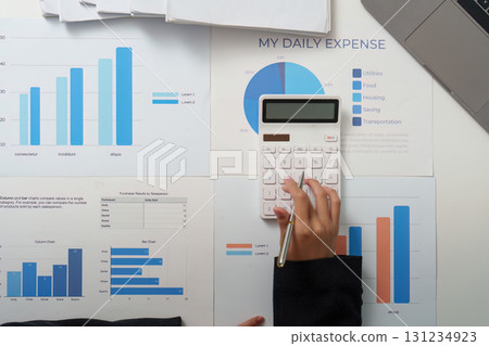 Daily Expense Management. Individual using calculator for daily expense tracking with financial charts. Daily Expense Management. Individual using calculator for daily expense tracking with financial charts. 131234923