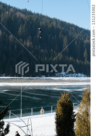 Thrill seeker descends from a snowy mountain into the icy waters of a serene lake surrounded by majestic evergreen forests 131235002