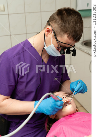 Dentist performing a pediatric dental examination with care in a modern clinic during a bright afternoon while ensuring comfort and safety for the young patient Dentist performing a pediatric dental examination with care in a modern clinic during a bright afternoon while ensuring comfort and safety for the young patient 131235008