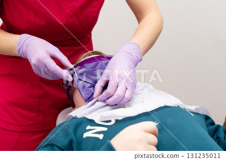 Surgical preparation in a medical setting showcasing a healthcare provider applying a mask to a patient's face during a dental procedure in a clinic Surgical preparation in a medical setting showcasing a healthcare provider applying a mask to a patient's face during a dental procedure in a clinic 131235011