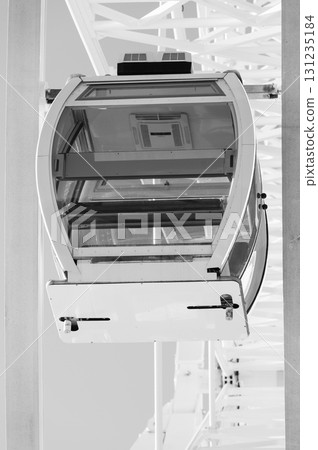 Beneath the towering ferris wheel, a solitary gondola dangles in the bright sunlight, waiting for visitors to enjoy panoramic views of the surrounding landscape 131235184