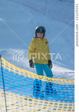 Young skier enjoying a bright winter day on a snowy slope surrounded by colorful safety netting in a ski resort setting Young skier enjoying a bright winter day on a snowy slope surrounded by colorful safety netting in a ski resort setting 131235351