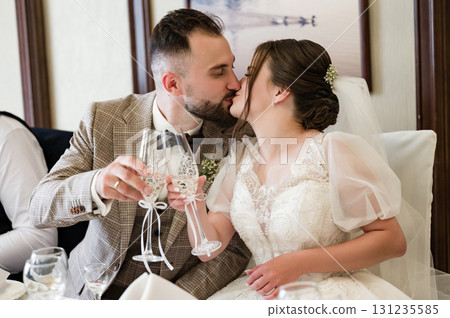 Newlyweds share a kiss and a celebratory toast, a tender moment captured at their wedding reception. Newlyweds share a kiss and a celebratory toast, a tender moment captured at their wedding reception. 131235585