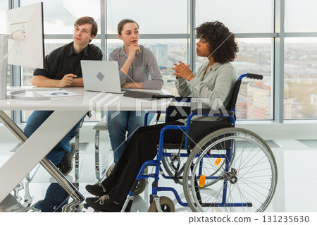 Teamwork brainstorm. Diverse multiracial colleagues woman in chair for people with disability working together. Group of people sitting in creative office discussing business. Young professional team 131235630