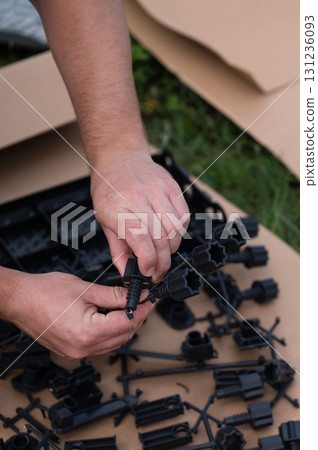 Person assembling black plastic parts outdoors. Detailed view of hands connecting pieces. Person assembling black plastic parts outdoors. Detailed view of hands connecting pieces. 131236093