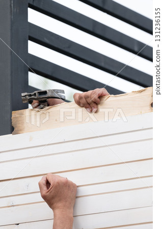 Workers install boards for a solid wall during the construction of a gazebo in the garden. Workers install boards for a solid wall during the construction of a gazebo in the garden. 131236155
