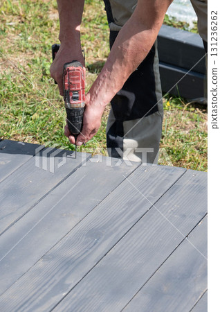 The craftsman uses a screwdriver to tighten the screws that secure the floor to the base of the gazebo. The craftsman uses a screwdriver to tighten the screws that secure the floor to the base of the gazebo. 131236262