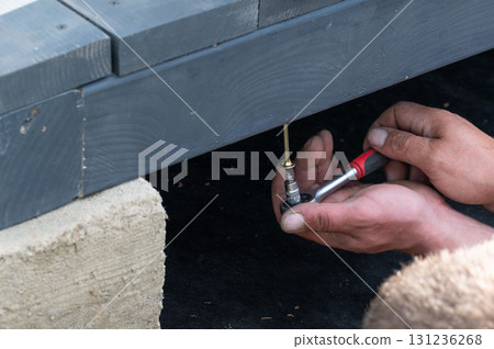 A man manually tightens a screw into the gazebo support to secure the floor to the frame. 131236268