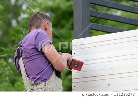 The craftsman screws a wooden board to a beam. 131236278