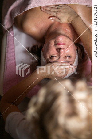 Close up of a mature woman lying on a treatment bed with a towel while a professional therapist performs a relaxing chest massage. Spa wellness and beauty treatment concept highlighting relaxation 131236523