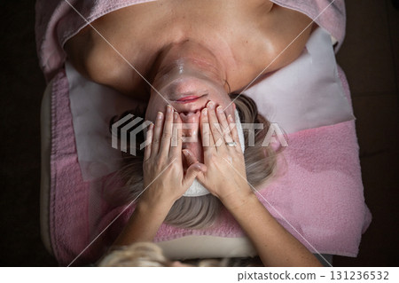 Close up of a mature woman receiving a relaxing facial massage from a professional female therapist in a modern spa. The client lies on a treatment bed with a towel and headband, enjoying skincare Close up of a mature woman receiving a relaxing facial massage from a professional female therapist in a modern spa. The client lies on a treatment bed with a towel and headband, enjoying skincare 131236532