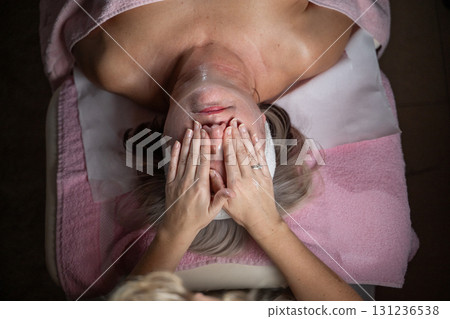 Close up of a mature woman receiving a relaxing facial massage from a professional female therapist in a modern spa. The client lies on a treatment bed with a towel and headband, enjoying skincare Close up of a mature woman receiving a relaxing facial massage from a professional female therapist in a modern spa. The client lies on a treatment bed with a towel and headband, enjoying skincare 131236538