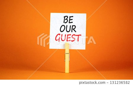 Be our guest symbol. Concept words Be our guest on beautiful white paper on wooden clothespin. Beautiful orange background. Business and be our guest concept. Copy space. 131236582