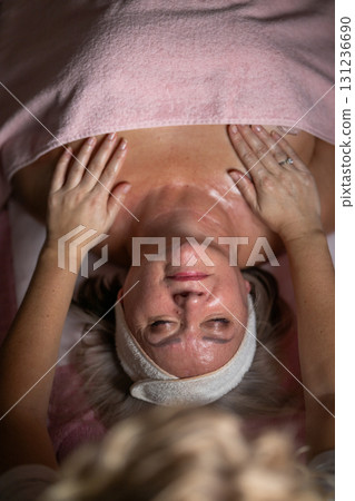 Close up of a mature woman lying on a treatment bed with a towel while a professional therapist performs a relaxing chest massage. Spa wellness and beauty treatment concept highlighting relaxation 131236690