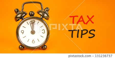 Tax tips symbol. Concept word Tax tips on beautiful orange paper. Beautiful black alarm clock. Beautiful orange paper background. Business tax tips concept. Copy space. Tax tips symbol. Concept word Tax tips on beautiful orange paper. Beautiful black alarm clock. Beautiful orange paper background. Business tax tips concept. Copy space. 131236737