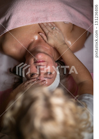 Close up of a mature woman lying on a treatment bed with a towel while a professional therapist performs a relaxing chest massage. Spa wellness and beauty treatment concept highlighting relaxation 131236806