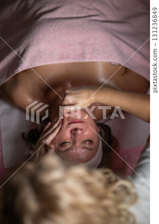 Close up of a mature woman lying on a treatment bed with a towel while a professional therapist performs a relaxing chest massage. Spa wellness and beauty treatment concept highlighting relaxation 131236849