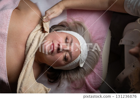 Close up of a mature woman receiving a relaxing facial massage from a professional female therapist in a modern spa. The client lies on a treatment bed with a towel and headband, enjoying skincare Close up of a mature woman receiving a relaxing facial massage from a professional female therapist in a modern spa. The client lies on a treatment bed with a towel and headband, enjoying skincare 131236876
