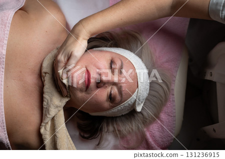 Close up of a mature woman receiving a relaxing facial massage from a professional female therapist in a modern spa. The client lies on a treatment bed with a towel and headband, enjoying skincare Close up of a mature woman receiving a relaxing facial massage from a professional female therapist in a modern spa. The client lies on a treatment bed with a towel and headband, enjoying skincare 131236915