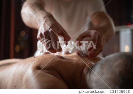 Close up of therapist applying cupping therapy on male clients back during wellness and rehabilitation treatment, traditional alternative medicine for relaxation and pain relief. 131236998