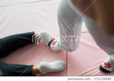 Close up of physiotherapist assisting an older woman by holding her legs during a rehabilitation exercise on a mat. Physiotherapy session concept emphasizing mobility recovery, strength training, and 131236999