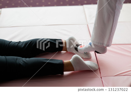 Close up of physiotherapist assisting an older woman by holding her legs during a rehabilitation exercise on a mat. Physiotherapy session concept emphasizing mobility recovery, strength training, and Close up of physiotherapist assisting an older woman by holding her legs during a rehabilitation exercise on a mat. Physiotherapy session concept emphasizing mobility recovery, strength training, and 131237022