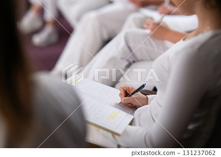 Close up of a student holding a pen and writing notes in a notebook during a professional training and education session in a wellness and therapy course 131237062