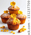 Four Golden Muffins Stacked on White with Yellow Flowers and Corn Kernels 131237709