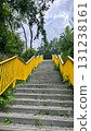 A set of concrete stairs leads upward, flanked by greenery. The handrails are painted bright yellow, contrasting with the natural surroundings 131238161