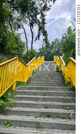 A set of concrete stairs leads upward, flanked by greenery. The handrails are painted bright yellow, contrasting with the natural surroundings 131238161