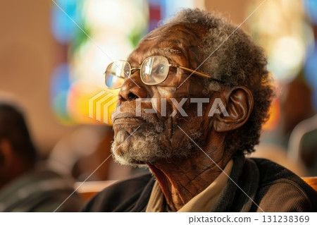 Elderly African American man reflecting quietly during church service, closeup portrait with soft lighting. 131238369